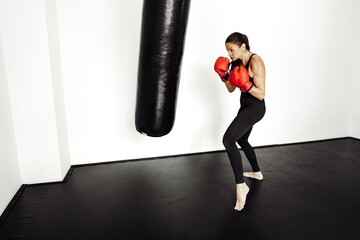 Woman athlete in red boxing gloves hits a pear in a gym