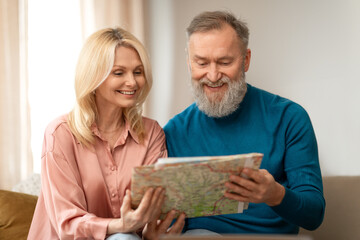 Cheerful Senior Couple Holding Paper Travel Map, Planing Vacation Indoor