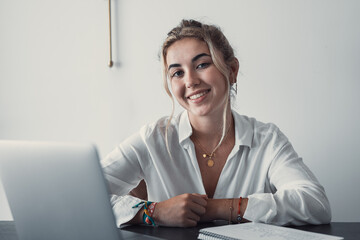 Good-looking millennial office employee student sitting at desk in front of laptop smiling looking at camera. Successful worker, career advance and opportunity, owner of prosperous business concept.