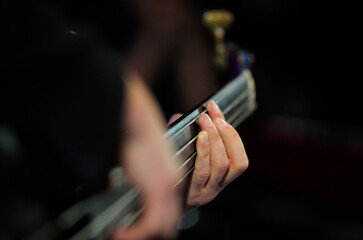 Musician hands playing electric bass guitar, striking a chord, close up