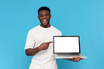 happy african american man in white t-shirt shows blank laptop screen on blue isolated background
