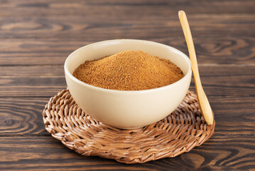 Bowl with heap of unrefined brown cane sugar Panela with wooden spoon on table.
