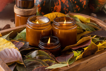 Soy candles burn in glass jars. Tree leaves. Comfort at home. Candle in a brown jar. Scent and light. Scented handmade candle. Aroma therapy. Autumn mood. Cozy home decor in fall. Festive decoration.