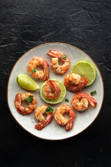 Shrimps, top shot. Cooked shrimp with lime on a white plate on a black stone table. Spanish cuisine