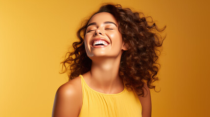 Young woman laughs against a yellow background.