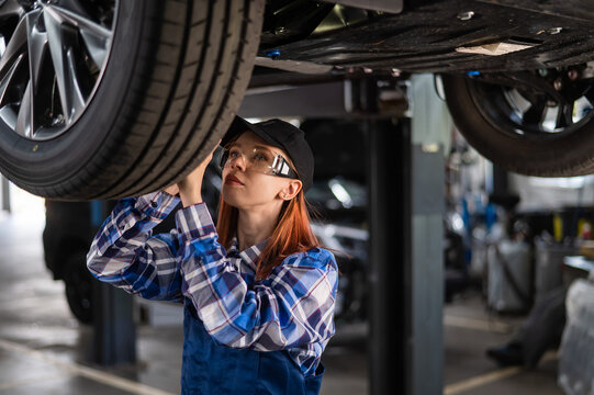 A female mechanic inspects a lifted car. A girl at a man's work.