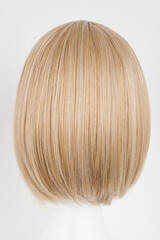Fototapeta premium Natural looking blonde fair wig on white mannequin head. Short hair cut on the plastic wig holder isolated on white background, back view.