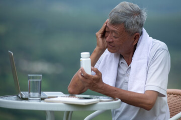 Asian old man is feeling unwell, like having a fever after exercising, sitting and holding medicine bottle reading label text about medical information, concept of healthy living in the elderly
