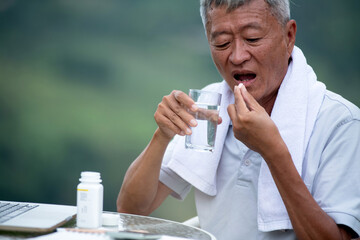 Asian old man hold pill and glass of fresh water, taking medicine daily pills for good health,...