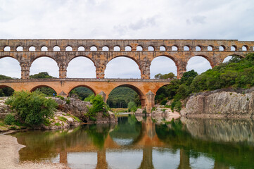 Fototapeta premium Panoramic view of ancient old Roman Aqueduct Pont du Gard ear Vers-Pon-du-Gard, Occitanie, France, Europe. Landmark over the River Gardon. Unesco world heritage site near Nimes, Languedoc-Roussillon