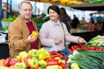 Mature married couple in casual clothes choosing organic bell peppers during date at local grocery market