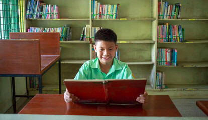 At the library, a young boy of Asian descent is deeply engrossed in reading a book during his break.