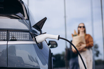 Woman doing grocery shopping while electric car charging © Petro