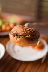 Male hand holding fresh baked hamburger with lettuce, arugula, onion, cheddar cheese, olive mayonnaise, cucumber, tomato and deer meat