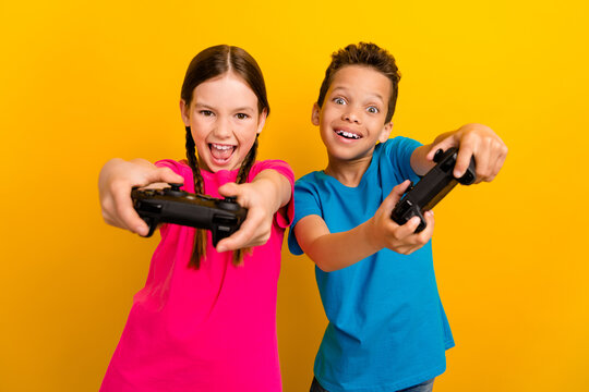 Photo of shocked pretty preteen schoolkids dressed t-shirts playing playstation game isolated yellow color background