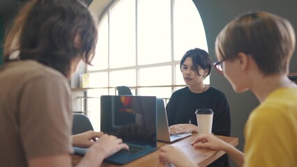 a group of students sit in a cafe and do a project on a laptop together. business concept of modern training and development. students discuss lifestyle their homework and eat fast food burgers