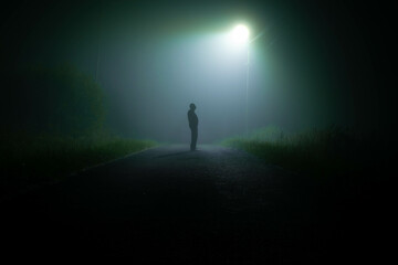A dark silhouette on a foggy road at night