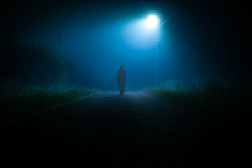 A dark silhouette on a foggy road at night