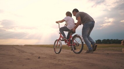 dad teaches son to ride a bike. happy family kid dream concept. the boy sat on bicycle for the first time, his father teaches boy to ride a bicycle. lifestyle dog runs with family, fun family pastime