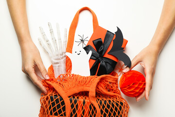 Halloween supplies in string bag and hands on white background, top view