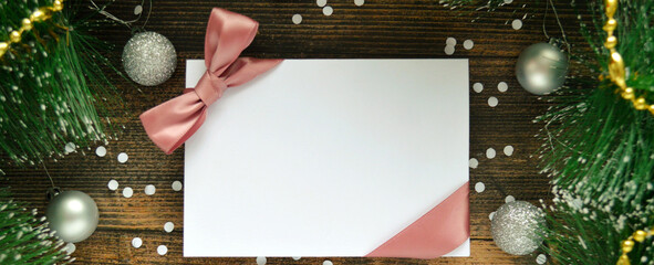 Blank white postcard with pink ribbon on dark wooden background with fir branches and silver...