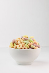 Colored flavored cereal rings in white bowl isolated on white with copy space
