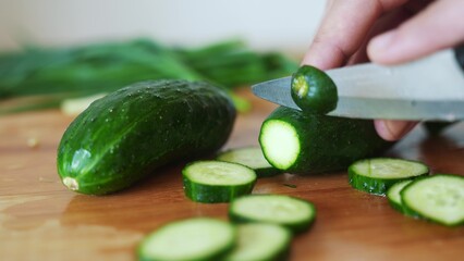 green cucumbers are cut with a knife in the kitchen. healthy food salad vegetables concept. close-up green cucumbers in the kitchen hands close-up cut into slices lifestyle