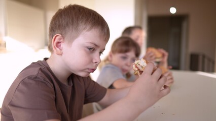 Obraz na płótnie Canvas children eat burgers. fast food burger. a group of small children in the kitchen greedily eat fast food burgers. big family small fun kids having breakfast in the morning in the kitchen eating burger