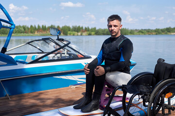 Full length portrait of adult man with disability using adaptive sports equipment outdoors on pier,...