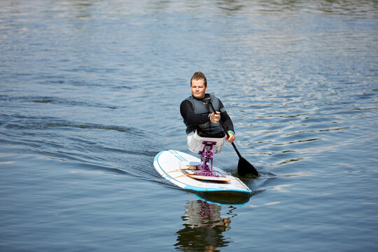 Full length portrait of young teenage boy with disability enjoying paddle boarding on water with adaptive sports equipment, copy space