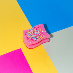 Pink sponge for dishes in the form of a birthday cake with sprinkles on yellow, blue and pink backgrounds. - 640221182