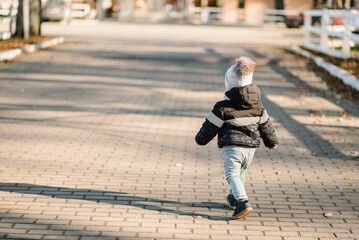 Child walking in park at sunset. Family spending time on vacation. Back view. Kid runs on street in nature. Concept of autumn holiday. Portrait of baby, toddler. Space for text. Place for advertising.