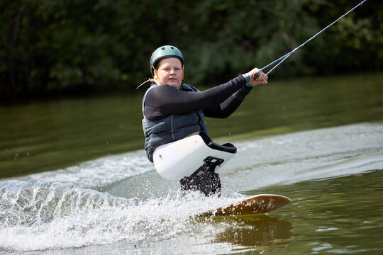 Action portrait of young man with disability enjoying fast speed wakeboarding on water with adaptive equipment, copy space