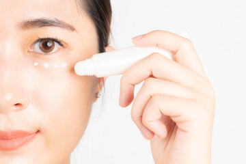 Smiling asian woman appying eye cream tube for dark circles treatment and anti aging. Skin care...