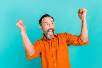 Portrait of overjoyed man dressed orange shirt look empty space raising fists up win lottery...