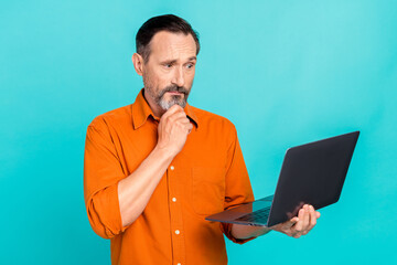 Fototapeta na wymiar Portrait of confused puzzled minded man dressed orange shirt look at laptop solving problem isolated on turquoise color background