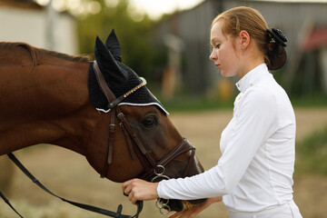 Obraz premium Jockey female rider portrait in white uniform holds bridle of dressage horse at stable