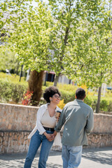 Fototapeta premium positive african american woman holding coffee to go near boyfriend on urban street