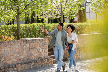 Obraz premium african american man with coffee to go pointing on urban street near cheerful girlfriend