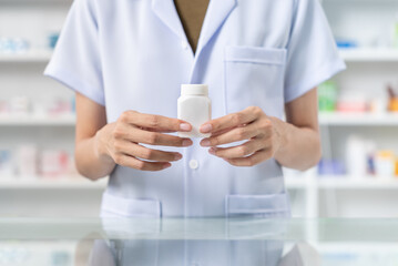 Fototapeta na wymiar Close up of female pharmacist hand holding pill bottle showing to camera, She wearing lab coat standing, trustworthy and proud of his work in the pharmacy drugstore. 