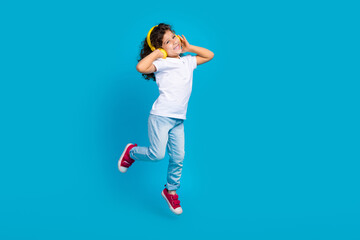 Photo of cheerful crazy kid girl jump listen pop music on headset isolated blue color background