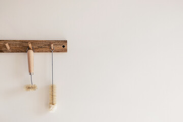Wood hook rack with sustainable cleaning brush hanging on a white wall on the modern style kitchen background. Smart organisation storage ideas. Eco friendly life..