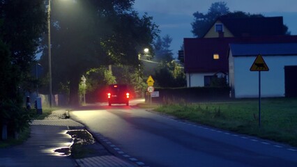 Obraz premium Car Driving Through Small Village Approaching Speed Limit Sign at Night