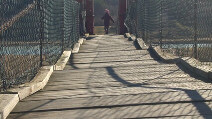Young Girl Walking alone on Wooden Suspension Footbridge Over a River