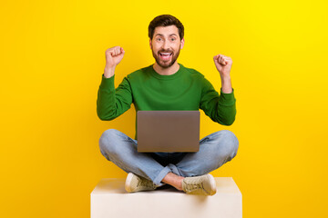 Full body cadre of overjoyed guy fists up approved new job after meeting with ceo sit box use laptop isolated on yellow color background