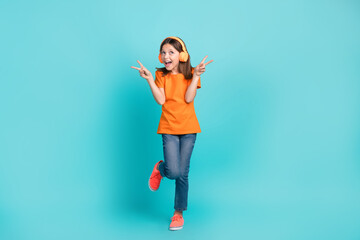Full length photo of overjoyed positive small girl wear orange stylish clothes hand v-sign epty space ad isolated on cyan color background
