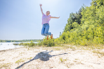 Fototapeta na wymiar Capture the essence of boundless joy with this exhilarating image. An attractive young millennial Caucasian woman leaps into the air, arms spread wide in sheer happiness during her summer holiday at