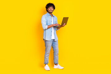 Full size photo of intelligent man dressed denim shirt stylish jeans holding laptop write email isolated on yellow color background