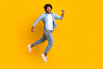 Fototapeta na wymiar Full length photo of hurrying funny guy dressed denim jacket jumping high running fast empty space isolated yellow color background