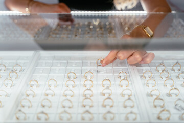 Luxury jewelry store concept. Close up of female hands put the ring while standing by large display...